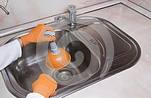 WomanÃ¢â¬â¢s hands with orange gloves cleaning sewer at kitchen faucet over sink. Close up of hand with plunger